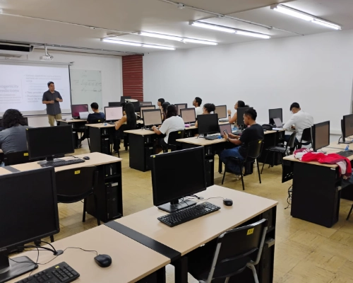 Estudiantes trabajando en equipos de cómputo en la sala Jürgen Tischer con docente al frente