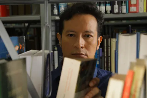 Joven buscando material bibliográfico en los estantes de la biblioteca